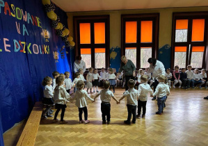 dzieci z grupy pierwszej tańczą w kole wraz z nauczycielem