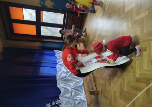 dziecko wraz z nauczycielką ubiera Mikołaja z papieru