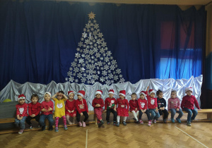 dzieci z grupy pierwszej w mikołajkowych czapkach na tle świątecznej dekoracji