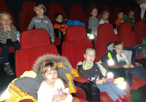 Dzieci siedzące na czerwonych fotelach w kinie.