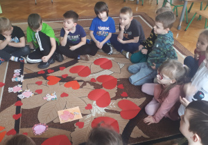 na zdjęciu dzieci z grupy ,,Misie” oglądające różne emblematy związane z walentynkami rozłożone na dywanie