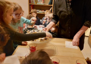 dzieci siedzą przy stolikach, kelnerka częstuje dzieci ciasteczkami
