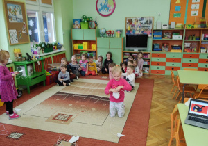 Dzieci siedzące w dwóch drużynach podczas konkursu: "kot łapie myszkę", nawijanie sznurka z papierową myszką.