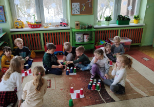 Dzieci siedzące na dywanie w małych zespołach układają sudoku z kolorowych kubeczków.
