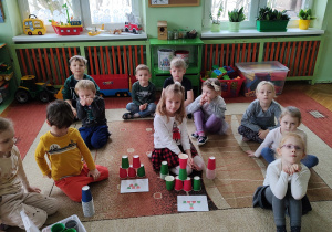 dzieci siedzące na dywanie podczas zadania polegającego na odwzorowaniu układu kubeczkowego.