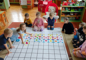 Dzieci siedzące wokół maty do kodowania. Układanie obrazków według kształtów i kolorów.