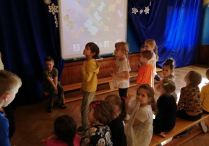 kilkoro dzieci stoi przed tablicą multimedialną, rozwiązują zadania na tablicy o tematyce dinozaurów