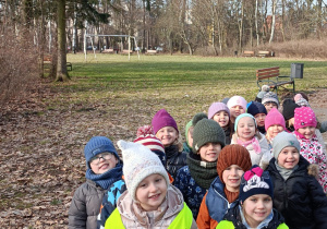 Na zdjęciu dzieci uśmiechnięte spacerują po parku.