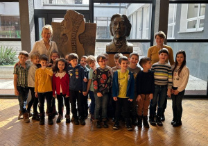 dzieci stoją przed popiersiem H. Wieniawskiego w holu szkoły muzycznej, w tle patio szkoły
