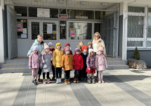 Na zdjęciu grupa dzieci wraz z nauczycielkami przed wejściem do szkoły.
