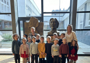 Na zdjęciu grupa dzieci z nauczycielkami przed popiersiem H. Wieniawskiego w holu szkoły muzycznej, w tle patio szkoły