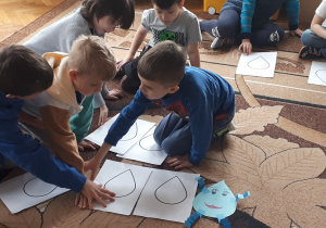 Zdjęcie przedstawia dzieci siedzące na dywanie i układające kropelki wody wydrukowane na papierze.