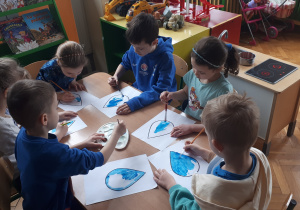 Na zdjęciu dzieci siedzące przy stolikach i wykonujące prace plastyczną – malowanie kropelki wody farbami