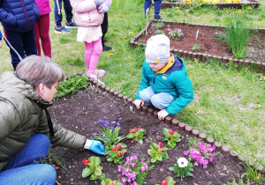 Na zdjęciu dzieci sadzą kwiaty w grupowym ogródku