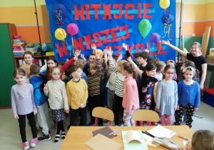 dzieci stoją w grupie przed tablicą z napisem "Witamy w naszej szkole"