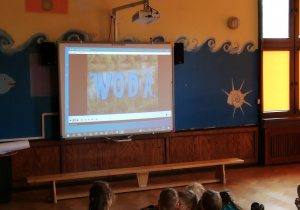 dzieci siedzą na sali i oglądają prezentację o tematyce oszczędzania wody na tablicy multimedialnej
