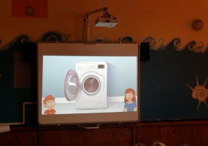 dzieci siedzą na sali i oglądają prezentację o tematyce oszczędzania wody na tablicy multimedialnej
