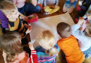 dzieci siedzą na podłodze i układają papierowe kropelki na kartonie tworząc obrazek