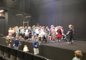 Dzieci na scenie teatru łapią rzucane przez aktorów kolorowe piórka