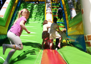 Na zdjęciu dzieci bawią się na dmuchańcach, skaczą i zjeżdżają na dmuchanej zjeżdżalni.