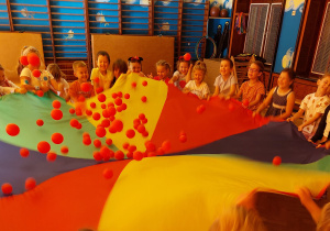 Dzieci podrzucają kolorowe piłeczki na chuście animacyjnej.