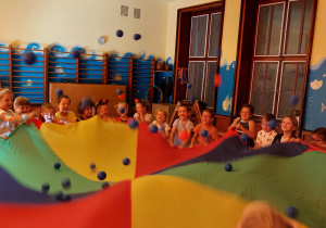 Dzieci podrzucają kolorowe piłeczki na chuście animacyjnej.