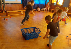 Dzieci zbierają w zespołach kolorowe piłeczki do odpowiednich koszyków.