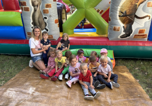 Na zdjęciu grupa maluszków z nauczycielką przy dmuchańcu w ogrodzie przedszkolnym.