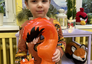 Na zdjęciu chłopiec z pomarańczowym balonem w kształcie cyfry 3.