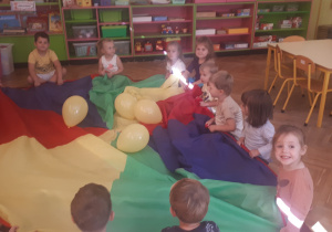 zdjęcie przedstawia dzieci z grupy ,,Misie” podczas zabawy z chustą animacyjną i balonami