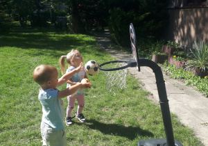 2-Na zdjęciu dzieci rzucające piłką do kosza na placu zabaw w przedszkolu