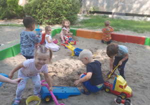 zdjęcie przedstawia dzieci bawiące się na dworze w przedszkolnej piaskownicy