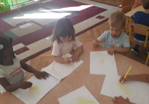 zdjęcie przedstawia dzieci siedzące przy stoliku malujące kredkami