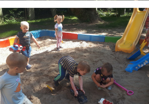 zdjęcie przedstawia dzieci bawiące się na dworze w przedszkolnej piaskownicy