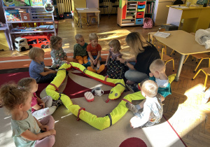 Na zdjęciu grupa dzieci wraz z nauczycielką bawią się na dywanie.