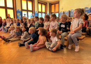 Na zdjęciu dzieci siedzą w skupieniu na sali gimnastycznej i oglądają przedstawienie Teatrzyku.