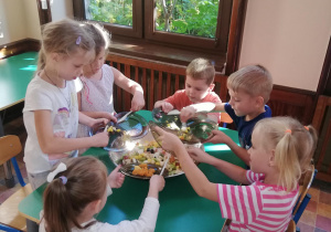 .dzieci przy stoliku, wrzucają do dużej misy pokrojone przez siebie owoce