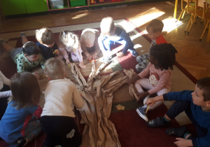 zdjęcie przedstawia dzieci z gr ,,Misie” układające drzewo na dywanie z wykorzystaniem gałęzi z szarego papieru.