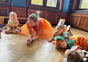 Na zdjęciu dzieci z nauczycielką przykucają na sali gimnastycznej podczas zabawy ruchowej.