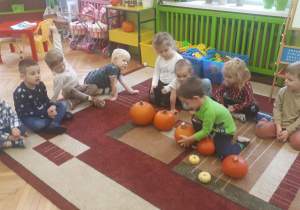 Na zdjęciu dzieci z grupy ,"Misie" siedzące na dywanie i uczestniczące w zabawie dydaktycznej z wykorzystaniem dyń.