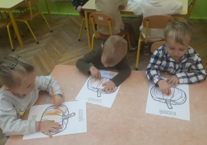 Na zdjęciu dzieci z grupy "Misie" siedzące przy stoliku i kolorujące obrazek dyni kredkami