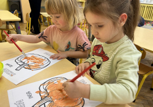 Na zdjęciu dwie dziewczynki malują rysunek dyni.
