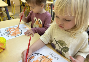 Na zdjęciu dwie dziewczynki malują rysunek dyni.