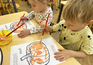 Na zdjęciu dwoje dzieci maluje rysunek dyni.