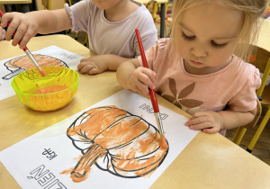 Na zdjęciu dzieci malują farbą kontury dyni.