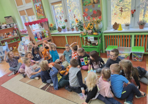 Na zdjęciu dzieci siedzą na dywanie i podaj sobie górą dynie z rąk do rąk.