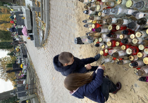 Chłopiec z dziewczynka zapalają znicze w miejscu pamięci zasłużonych Polaków na cmentarzu na Dołach.