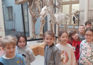 Na zdjęciu widać dzieci stojące na tle szkieletów zwierząt