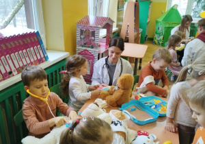Dzieci siedzące przy stolikach wykonują przykładowe zabiegi lekarskie na swoich pluszakach