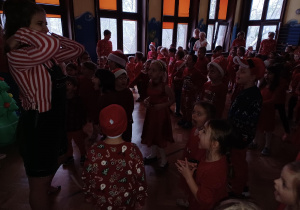 na zdjęciu dzieci w czerwonych, mikołajkowych strojach tańczące podczas zabawy mikołajkowej
